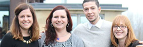 Three women and one man stood together smiling.